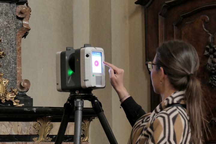 Mano sul display del laser scanner durante il rilievo di un altare dorato
